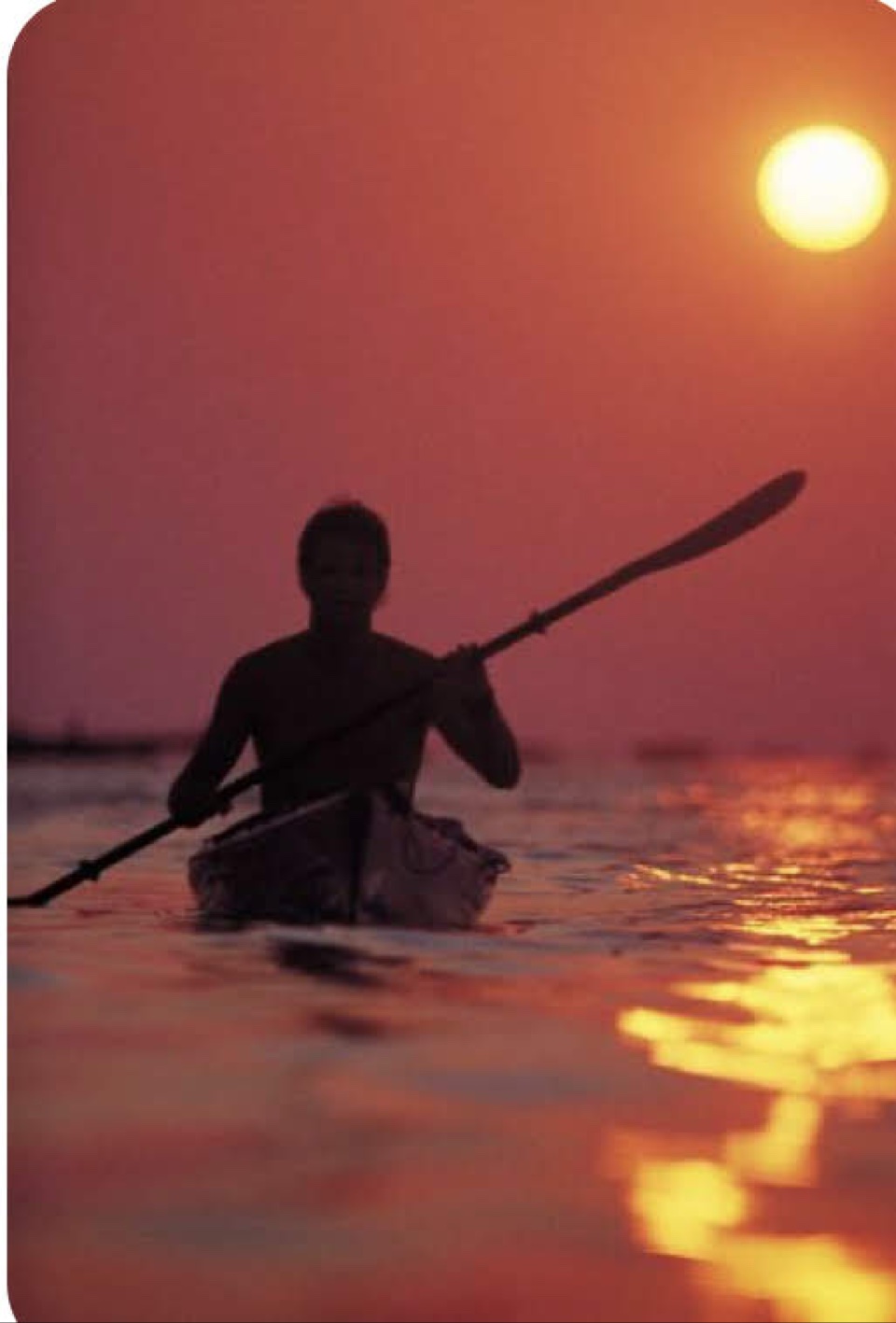 Kayaker silhouetted against an orange sunset