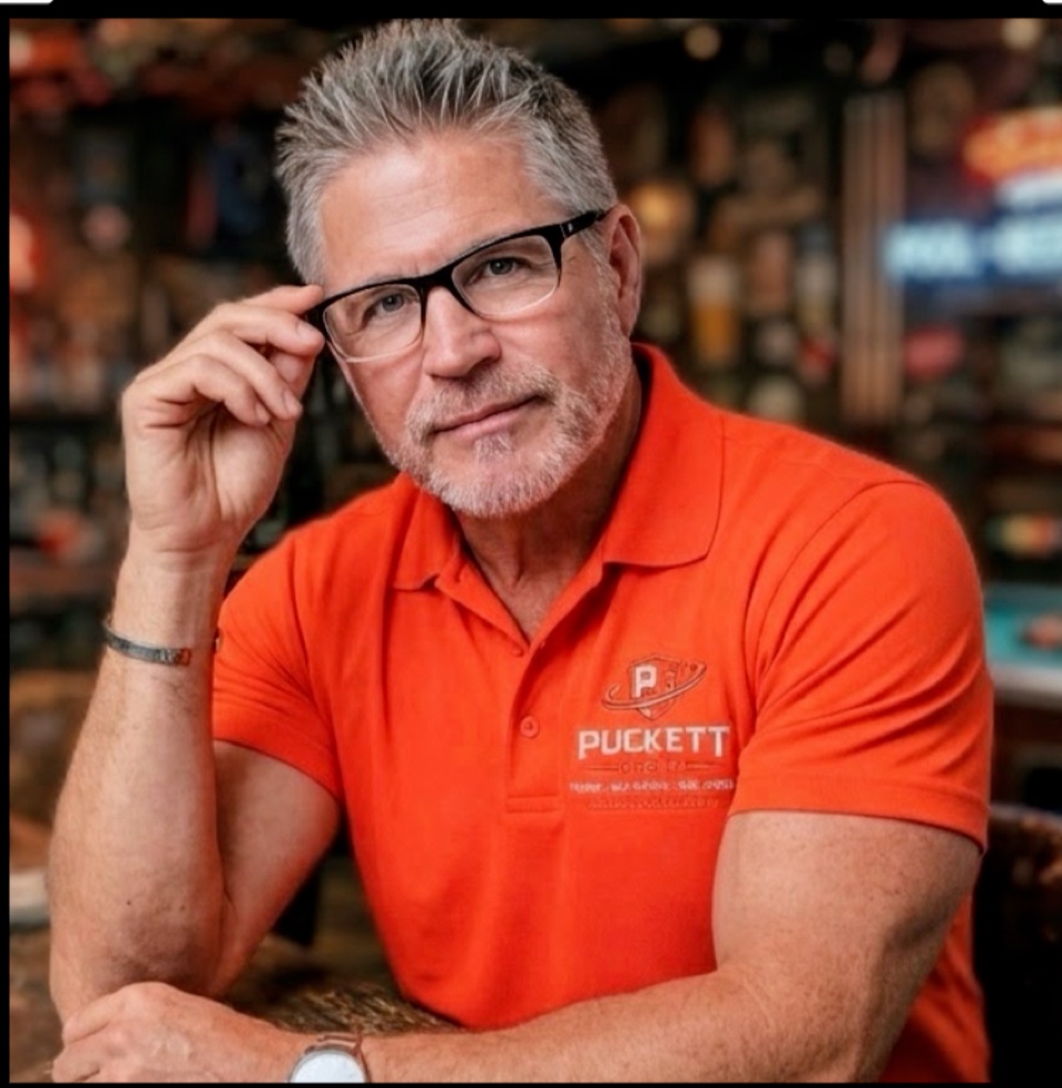 Steve Puckett adjusting his glasses in an orange Puckett Group polo